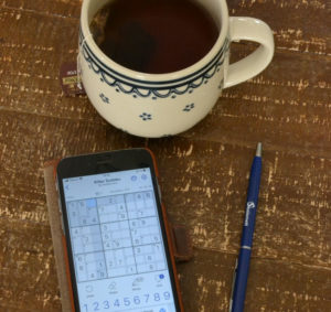 Bilde av mobil med sudoku, penn og kaffekopp